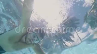 男子游泳面具游泳在透明的游泳池在热带棕榈背景。 戴护目镜的年轻人
